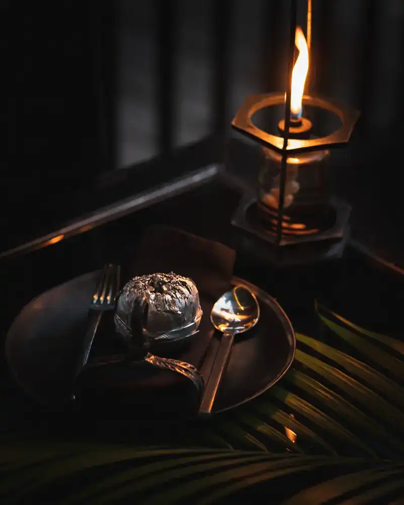 A table set with a silver covered dish and a lit oil lamp