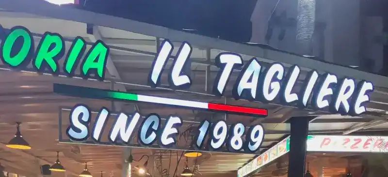 The lit shop sign at night: Pizzeria Il Tagliere, since 1989, with a green, white and red stripe