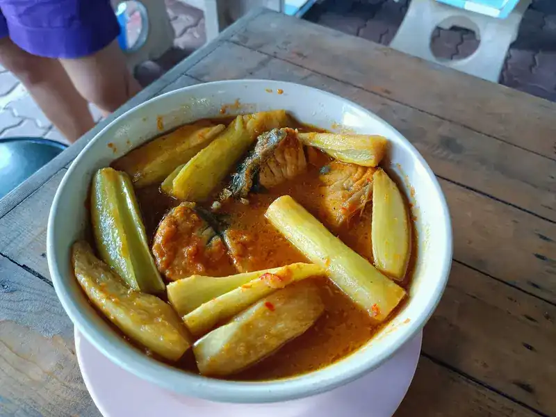 Orange fish curry with young shoots in a white bowl