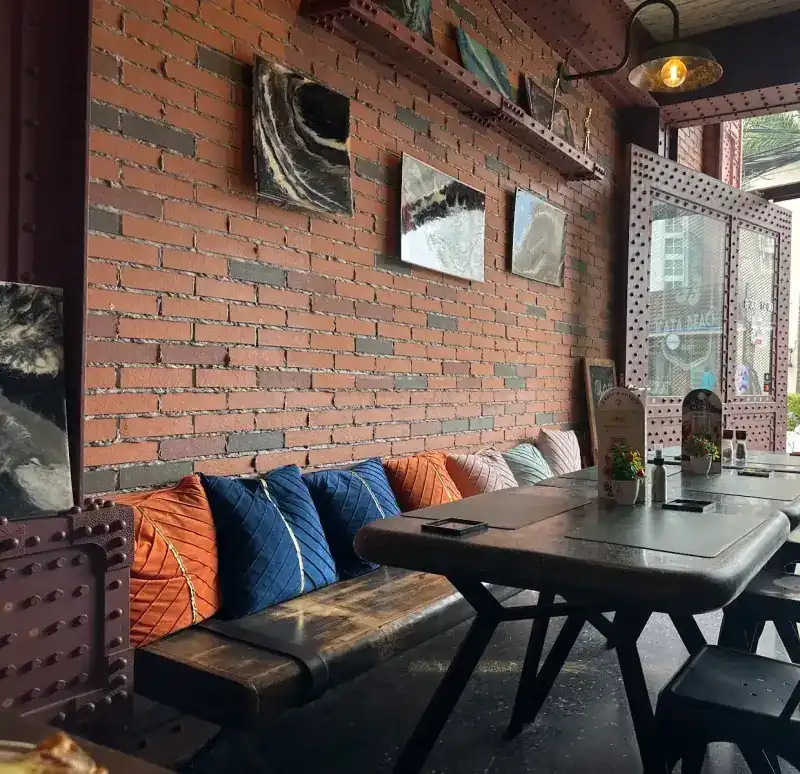 The brick wall inside, with a cushioned bench, paintings and tables by the open front
