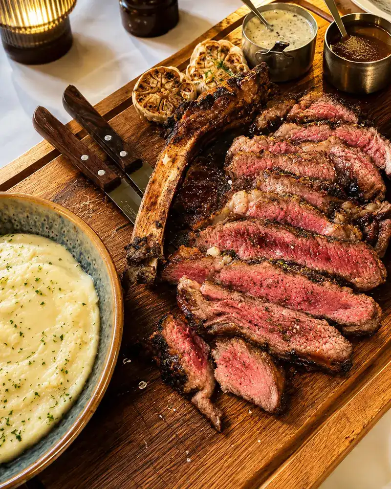 Sliced bone-in rib steak on a wooden board with mashed potato
