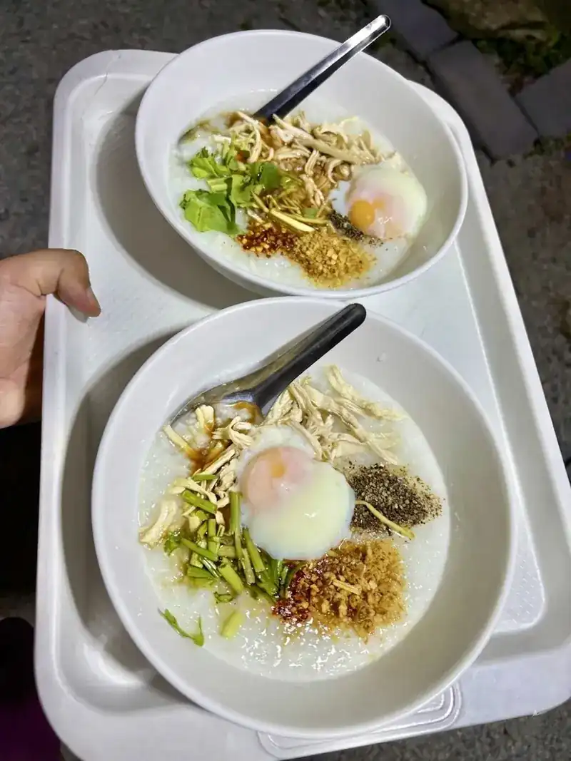 Two bowls of rice porridge with a soft egg and toppings on a tray