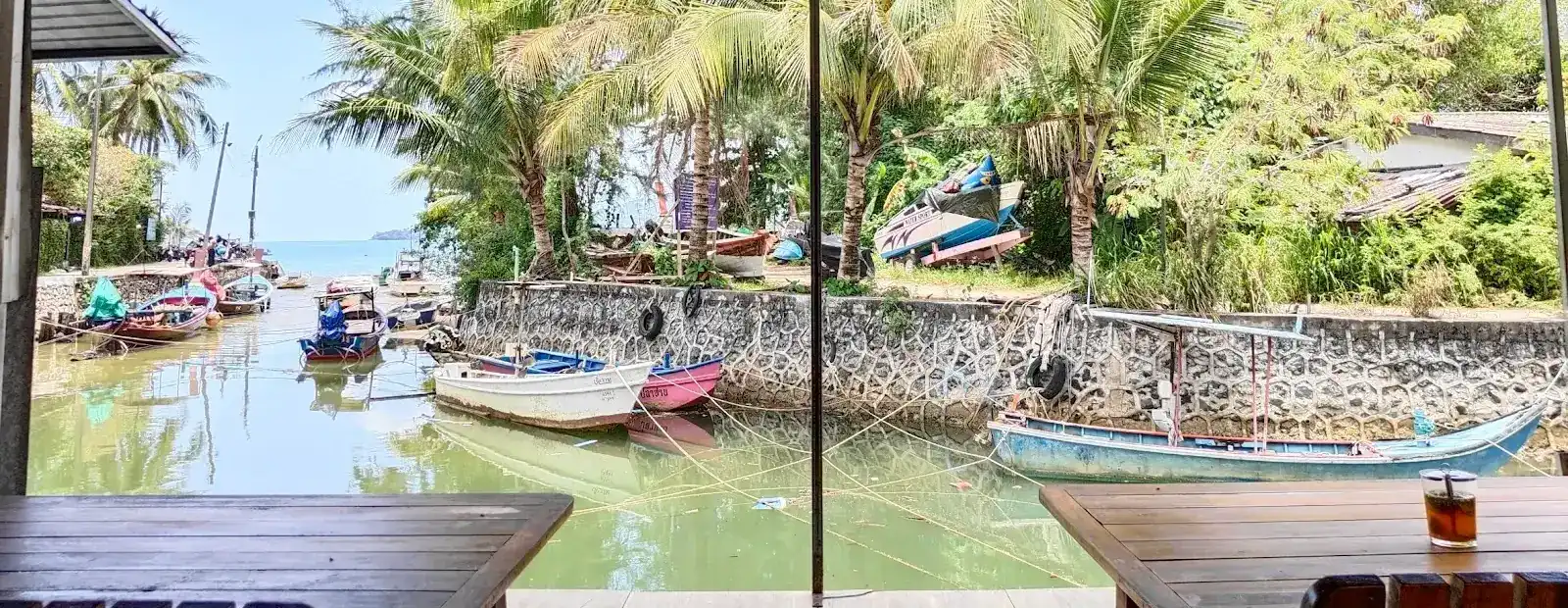 The canal seen from Kaeng Restaurang's tables: moored boats, palm trees and the sea at the far end