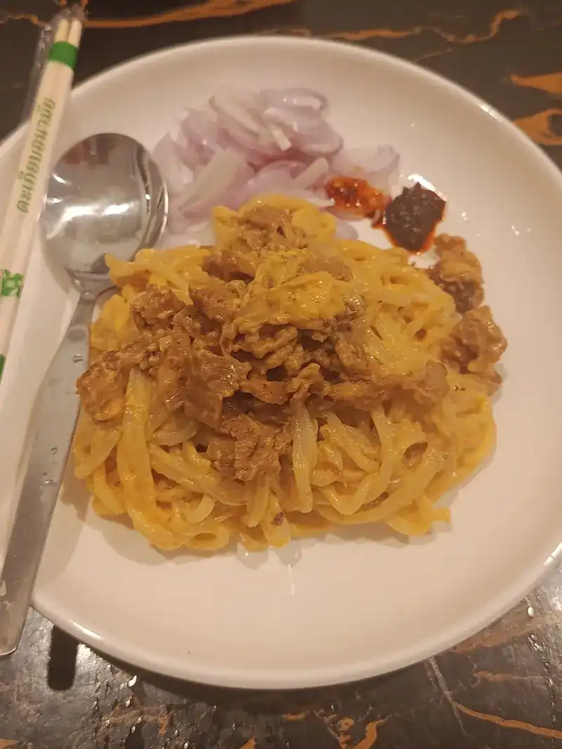 A plate of yellow noodles with a meat sauce and sliced shallots