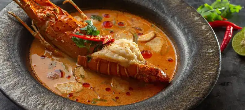 Tom yum soup with a whole lobster in a dark stone bowl