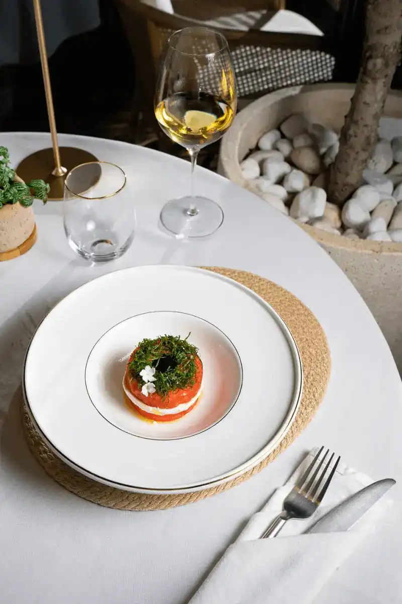 A small tower of red and white layers topped with herbs on a white plate