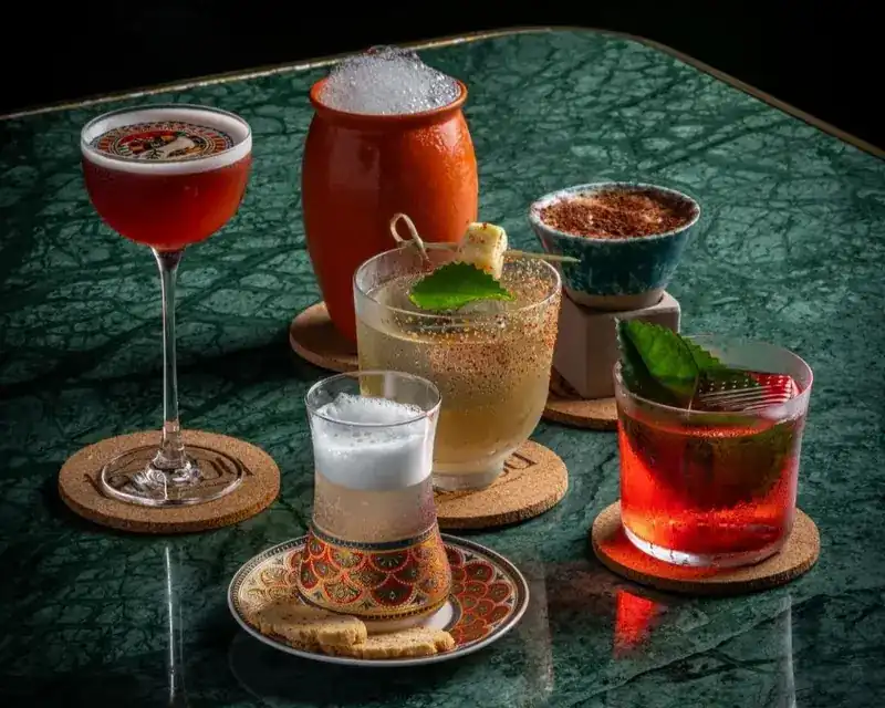 Five drinks on a green marble table, in a clay pot, a painted tea glass and stemmed glasses