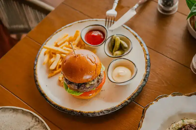 A burger with fries, pickles and two dips