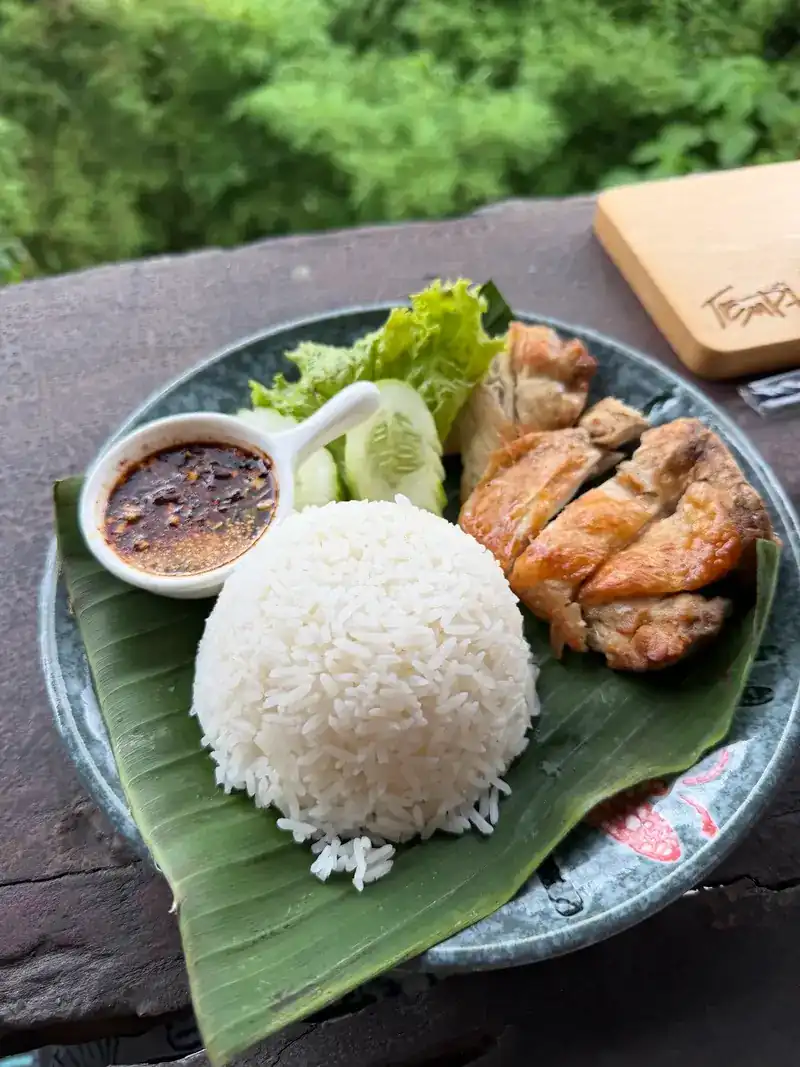 Grilled chicken with rice, cucumber and a dipping sauce on a banana leaf