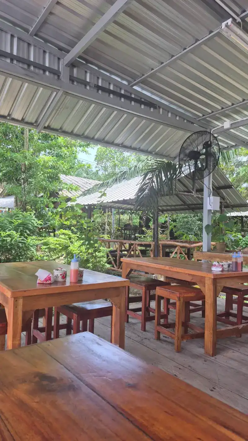The open-sided dining hall: wooden tables and stools under a metal roof, garden all round