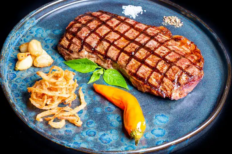 Steak with deep crosshatch grill marks, salt and pepper, roasted garlic and crispy onions on a blue plate