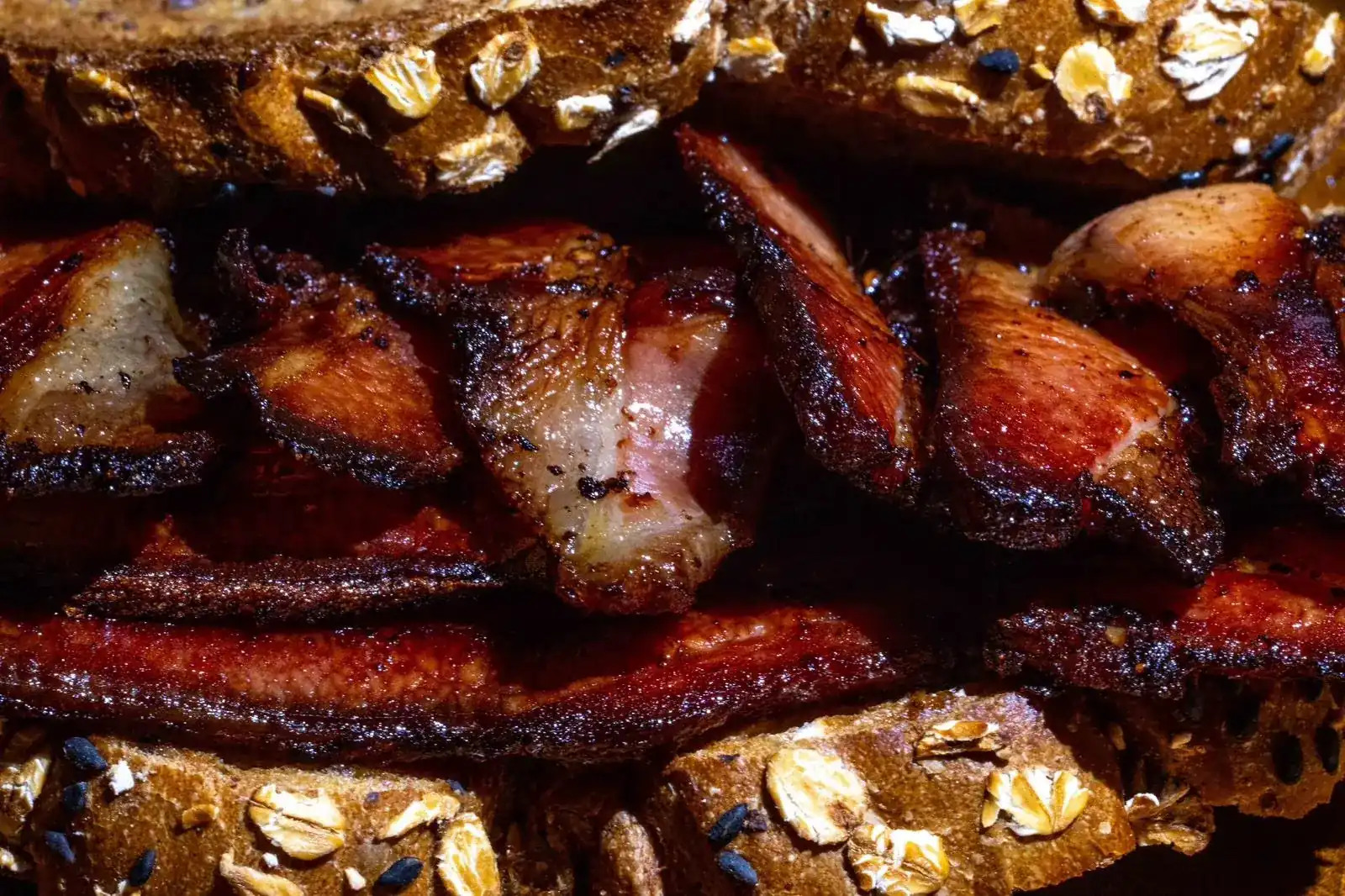 Thick slices of smoked bacon, charred at the edges, in toasted oat bread