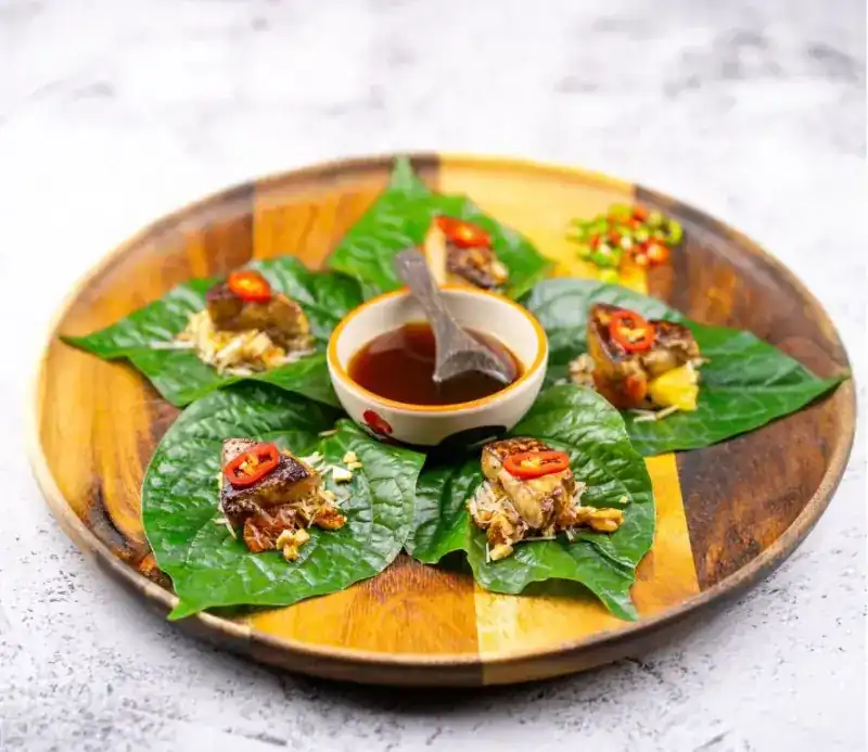 Miang foie gras on betel leaves, served on a wooden plate