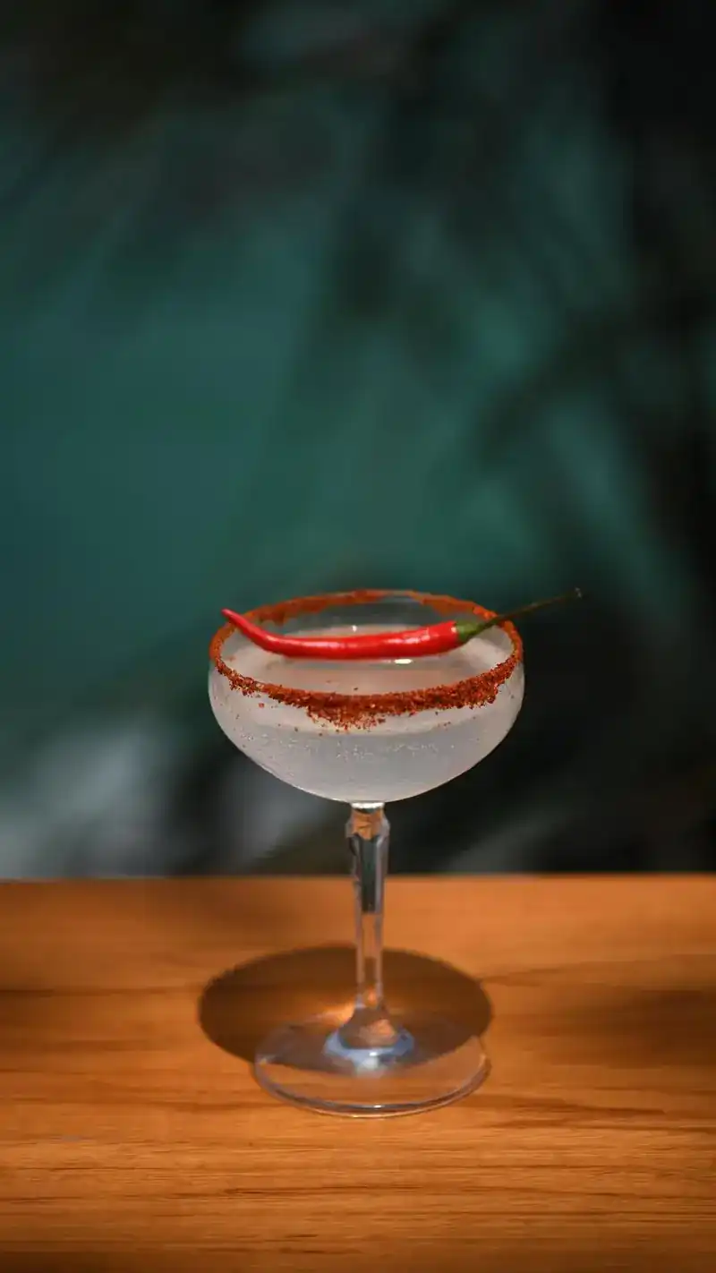 A coupe glass with a red chili on a chili-salt rim