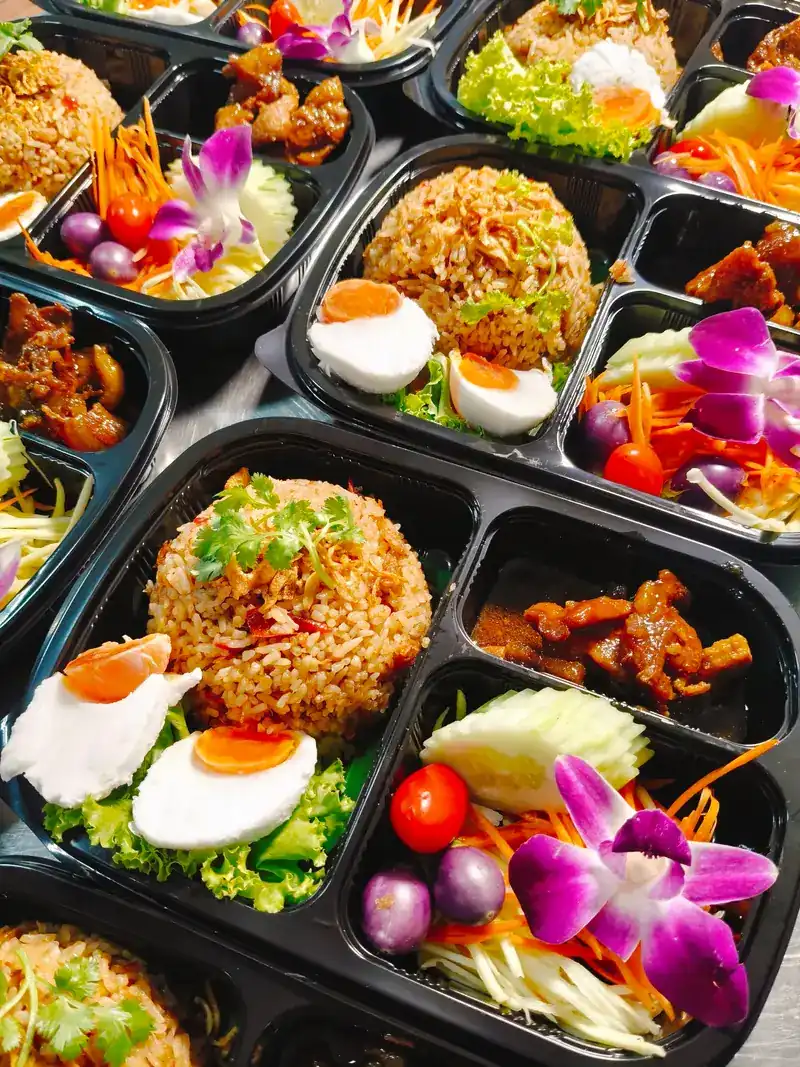 Boxed meals of fried rice with halved eggs, salad, cherry tomatoes and an orchid flower