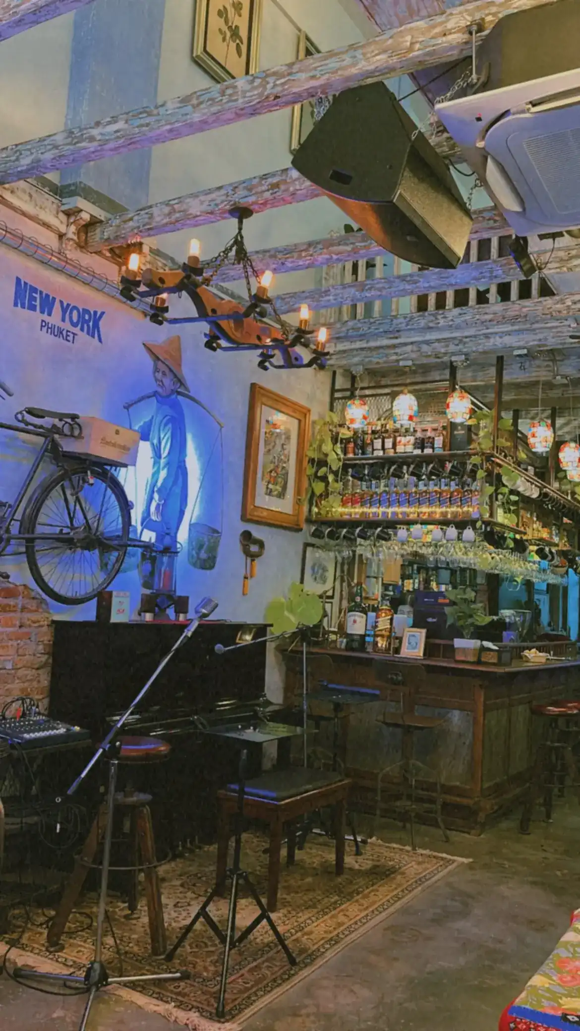 The bar and live-music corner under whitewashed beams, a mural of an old Phuket street vendor and stained glass lamps