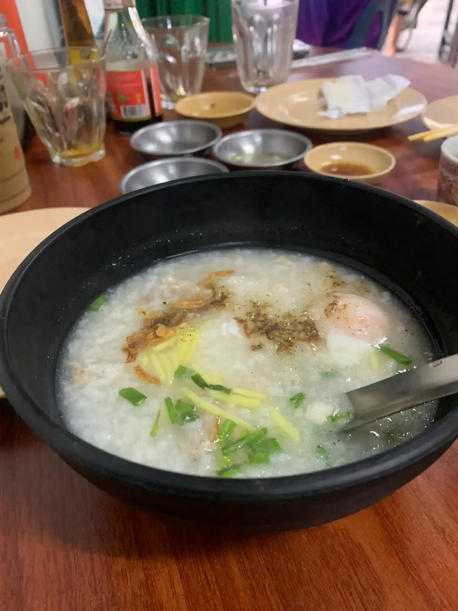 A bowl of rice porridge with ginger, spring onion, fried shallots and an egg