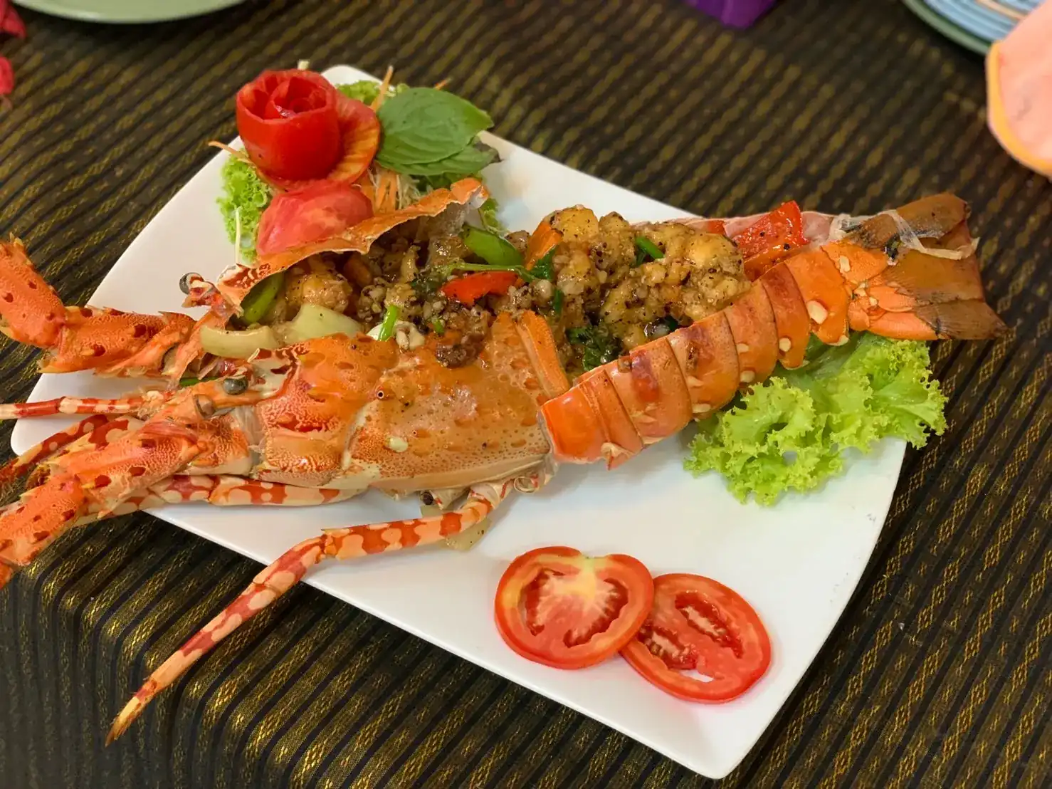 Grilled lobster split open and topped with garlic and black pepper, on a white plate