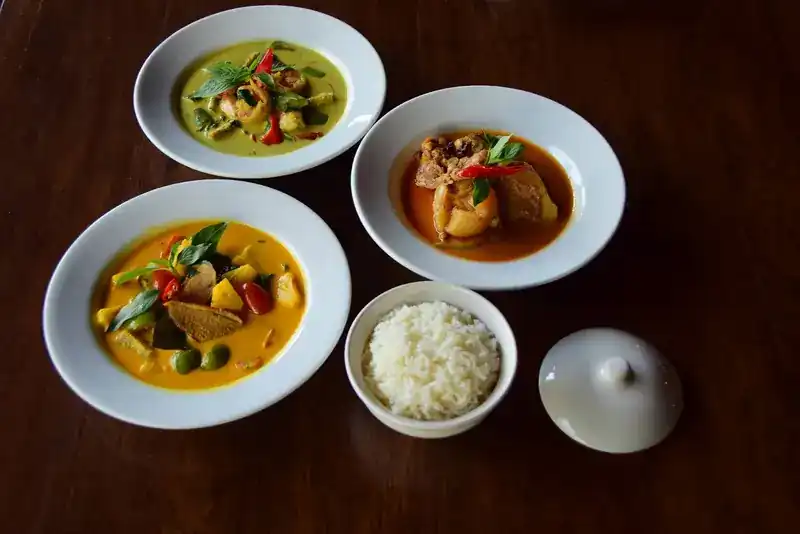 Green, red and yellow curries in white bowls with a bowl of steamed rice