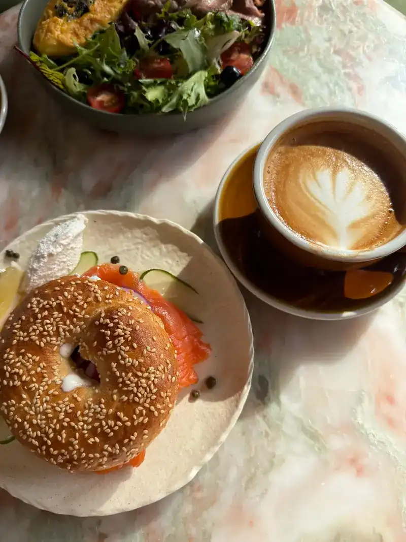 A sesame bagel with smoked salmon, a green salad and a cappuccino on a marble table