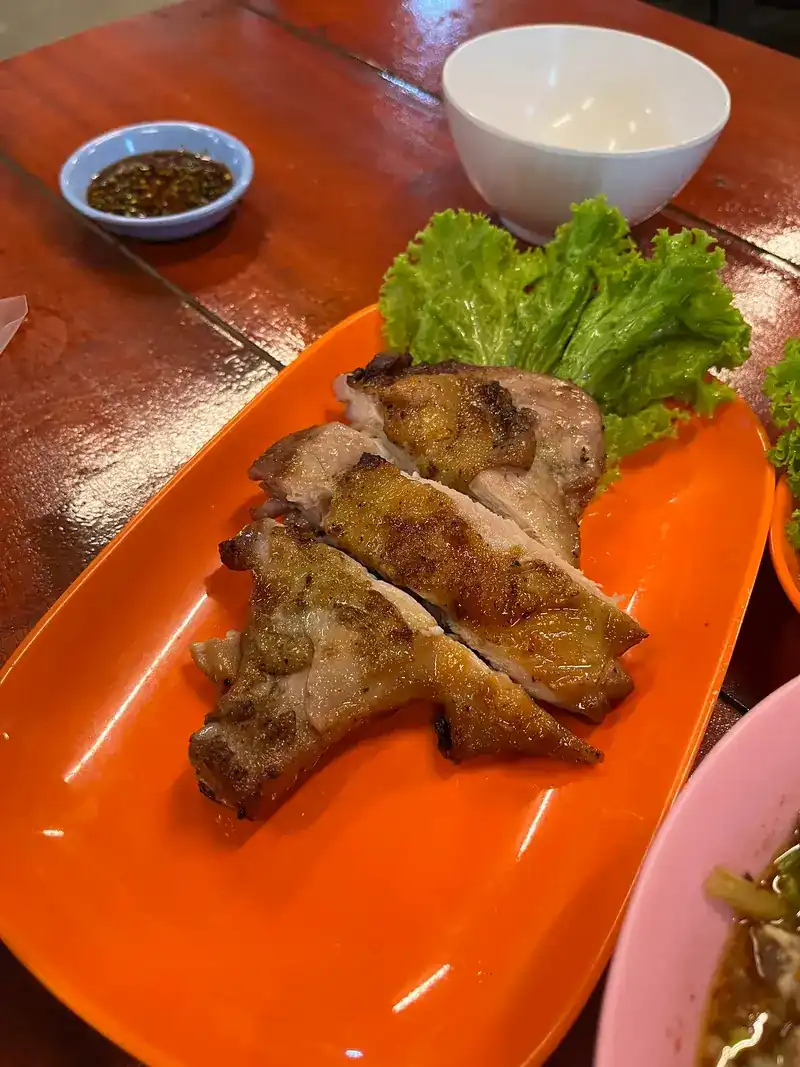 Grilled meat sliced on an orange plate with lettuce and a dish of chilli dip