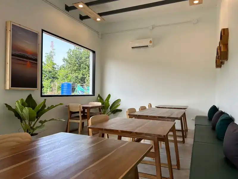 The dining room: wooden tables, a bench with green cushions, plants and a big window