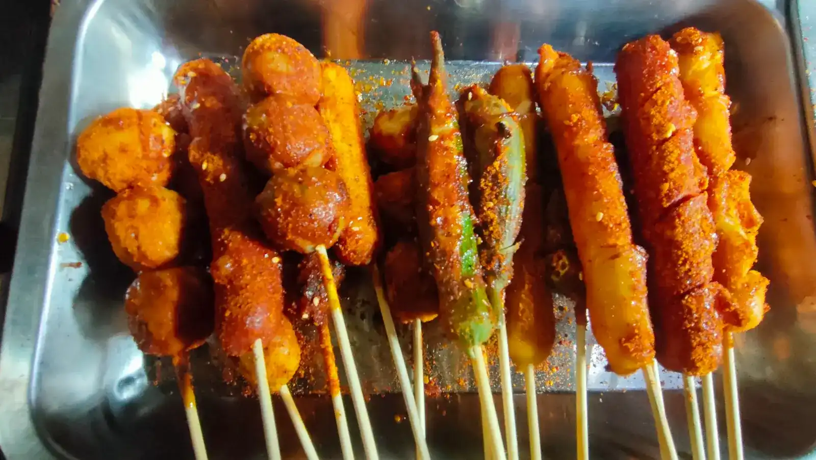 Grilled skewers dusted with red mala spice and sesame on a steel tray