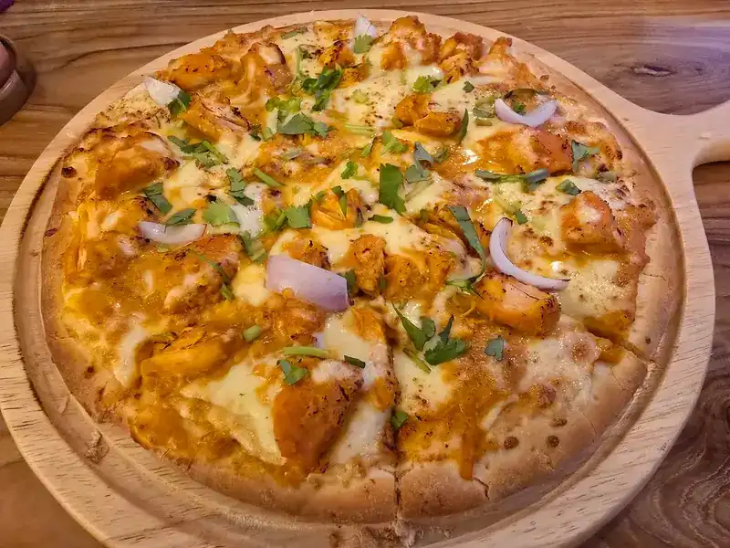 A pizza topped with chicken, red onion, melted cheese and fresh herbs