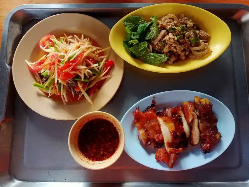 Som tam, larb with mint, grilled meat and a bowl of chilli dip on a tray