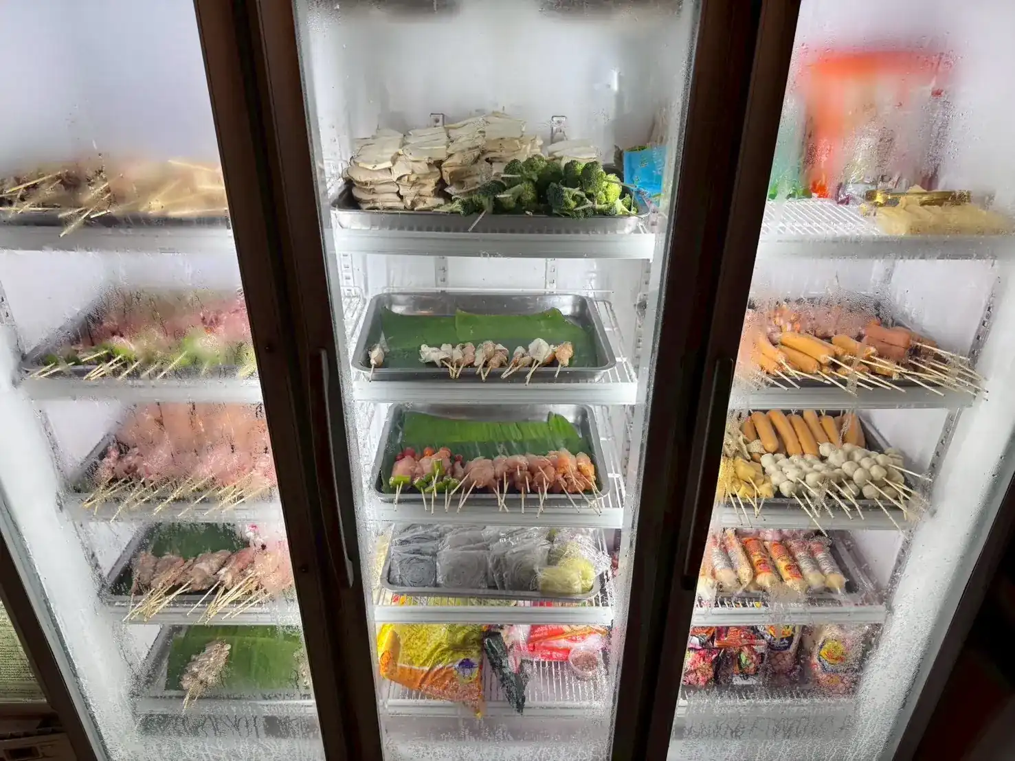 Glass-door fridge stacked with trays of raw skewers, ready to grill