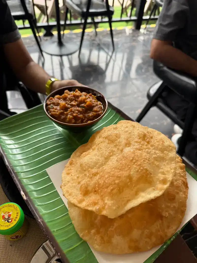 Two puffed bhature beside a bowl of chole on a leaf-green tray