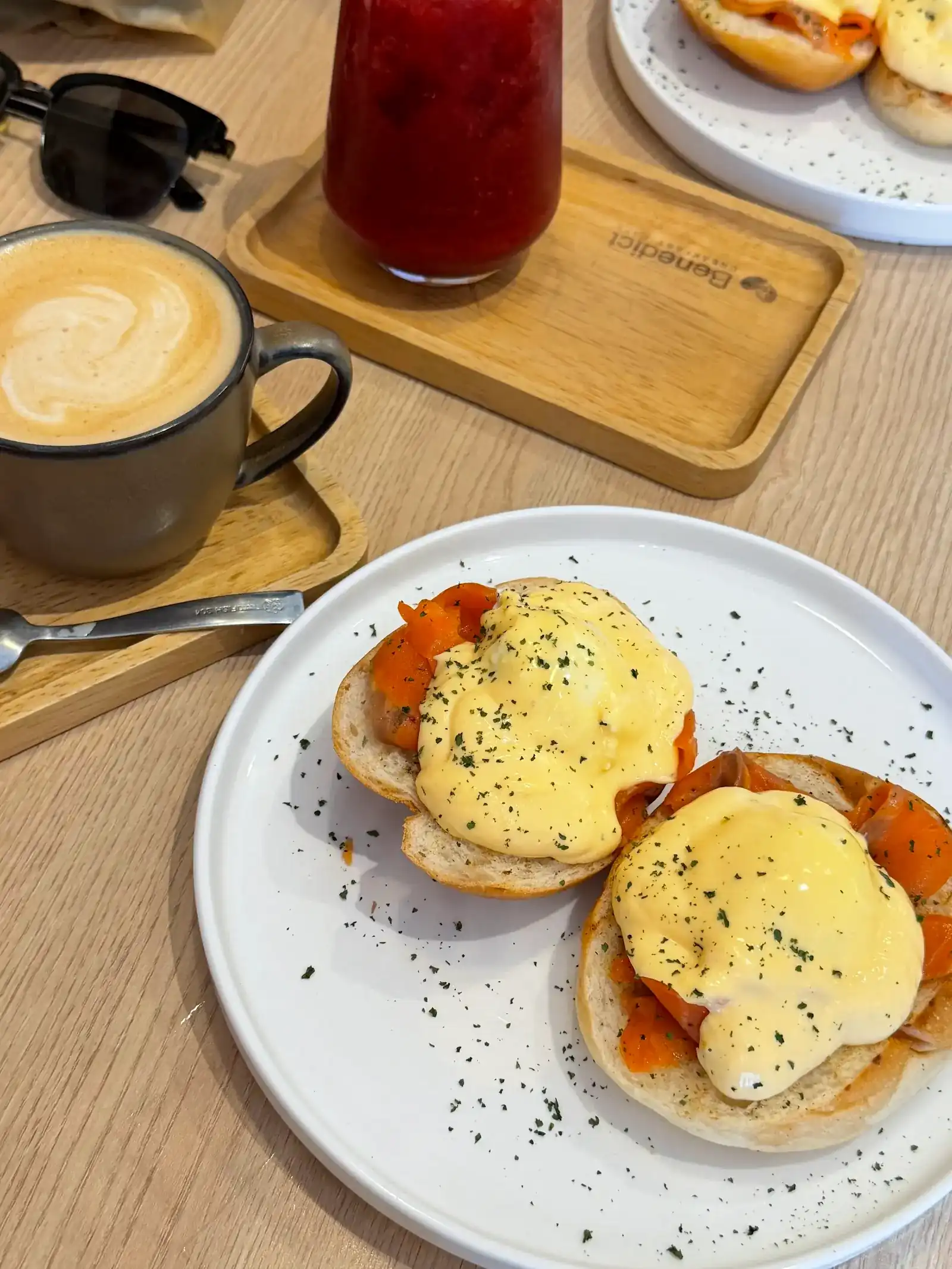 Eggs benedict with salmon and hollandaise on a white plate, with a coffee beside it