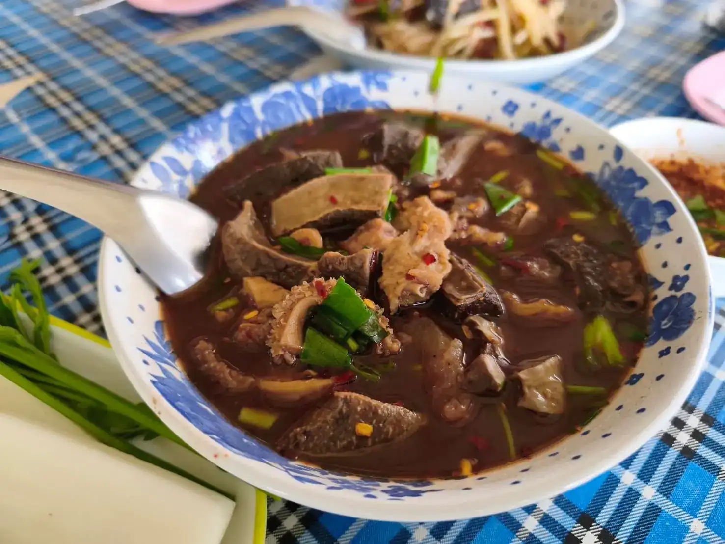 A bowl of soup with offal, chilli and spring onion on a blue checked tablecloth