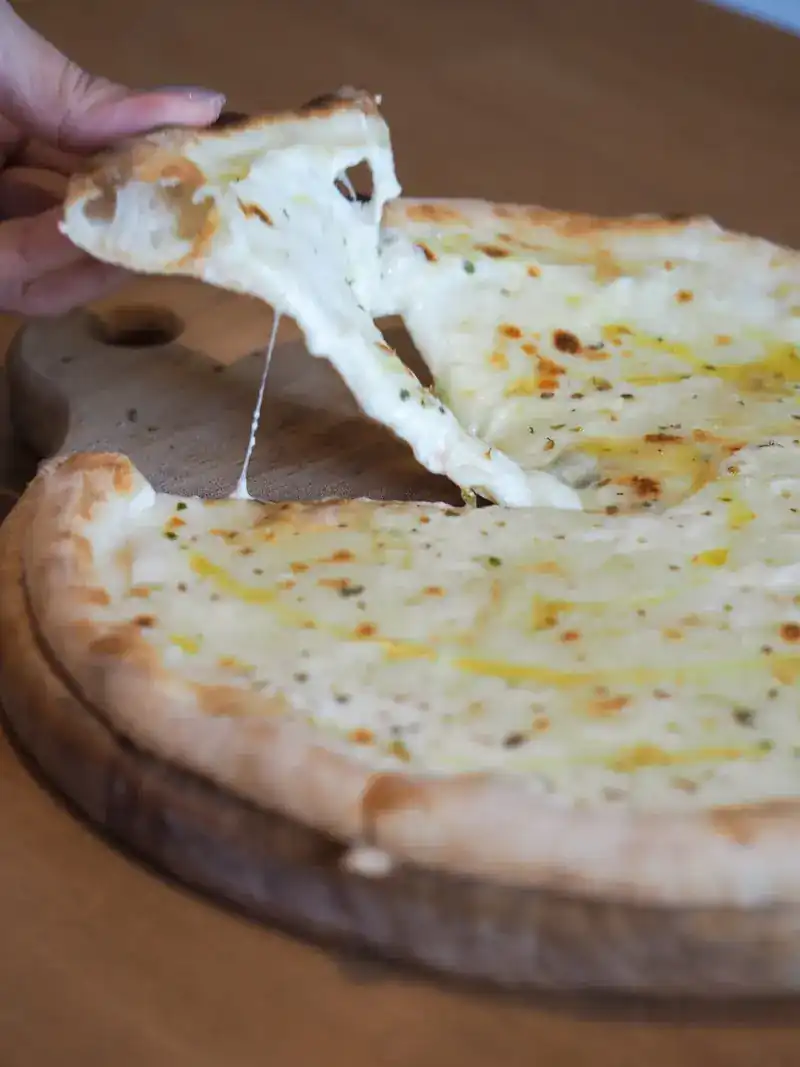 A slice of white cheese pizza being pulled away, the cheese stretching