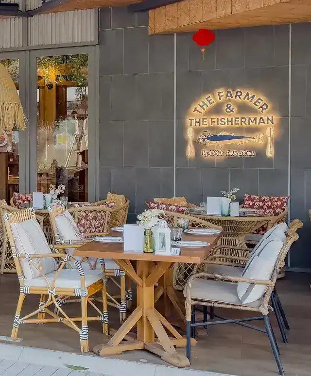 The terrace: rattan chairs and a wooden table in front of the lit sign of The Farmer & The Fisherman