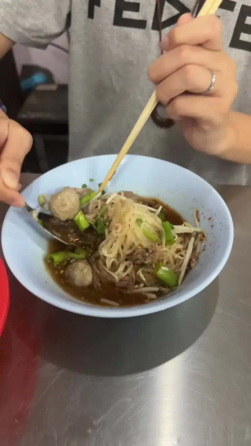 Lifting noodles from a bowl with meatballs and bean sprouts / คีบเส้นจากชามก๋วยเตี๋ยวใส่ลูกชิ้นและถั่วงอก