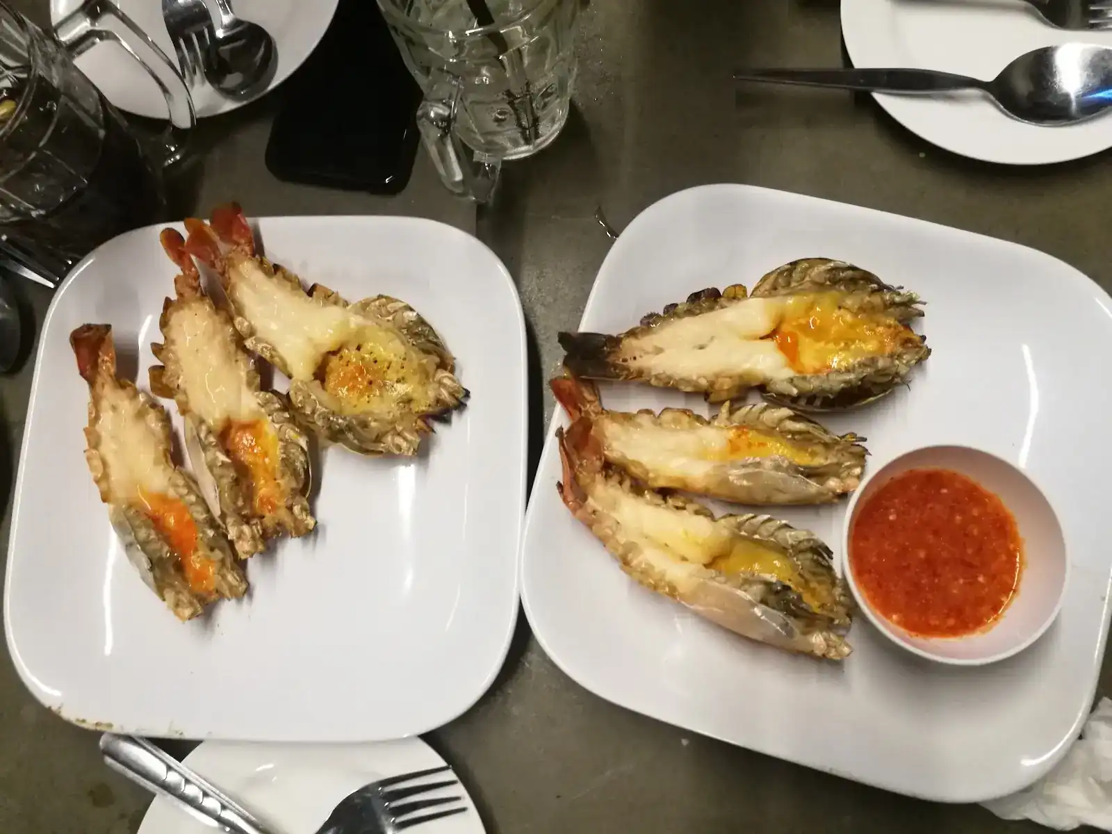 Grilled prawns split down the middle on two white plates, with a bowl of red chili dip