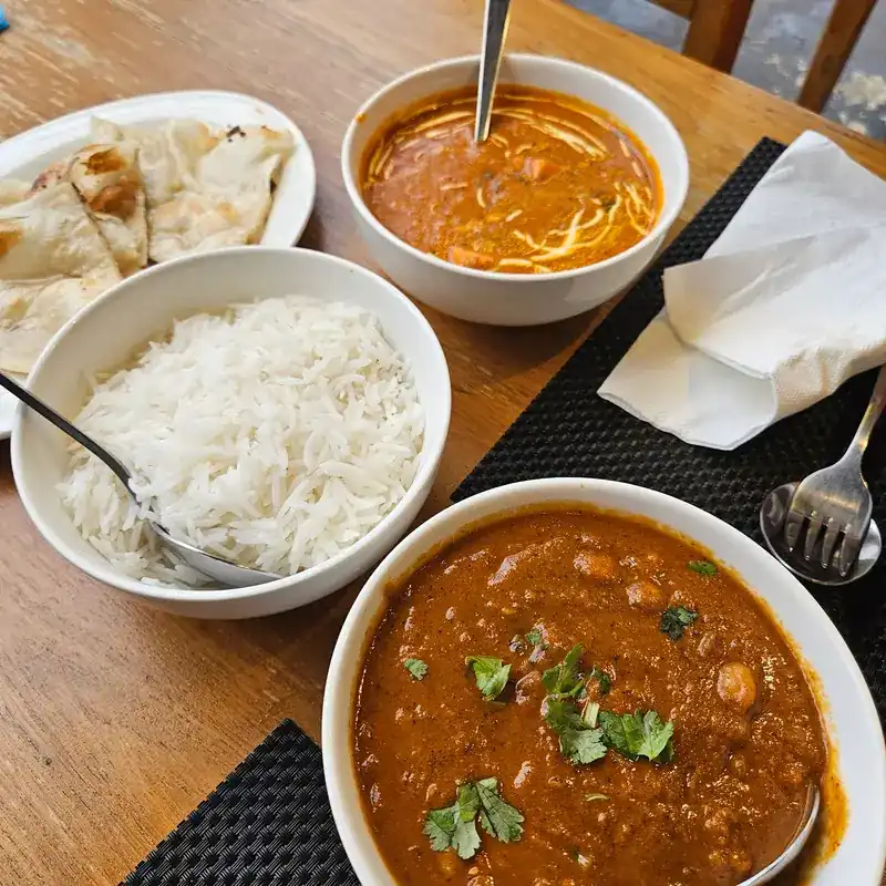 Chickpea curry, a creamy curry, plain rice and naan on a wooden table