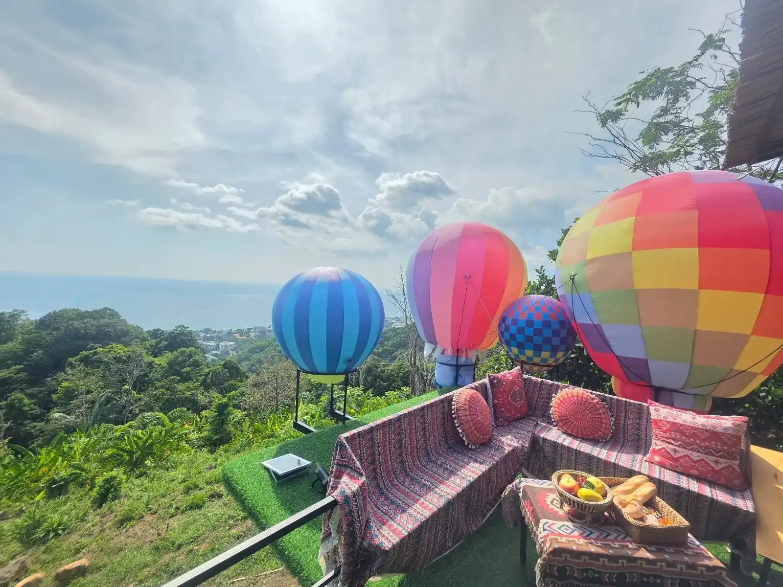 Hot air balloons and a cushioned corner sofa on the terrace, with forest and the sea beyond