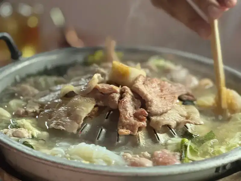 Pork sizzling on the domed pan with broth and cabbage around it