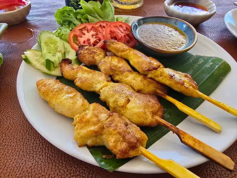 Grilled chicken skewers with peanut sauce, cucumber and tomato