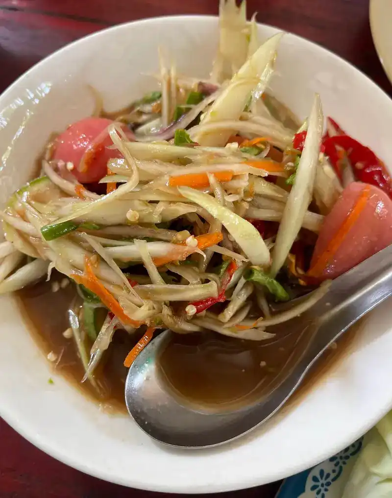 Green papaya salad with tomato and red chilli in a white bowl