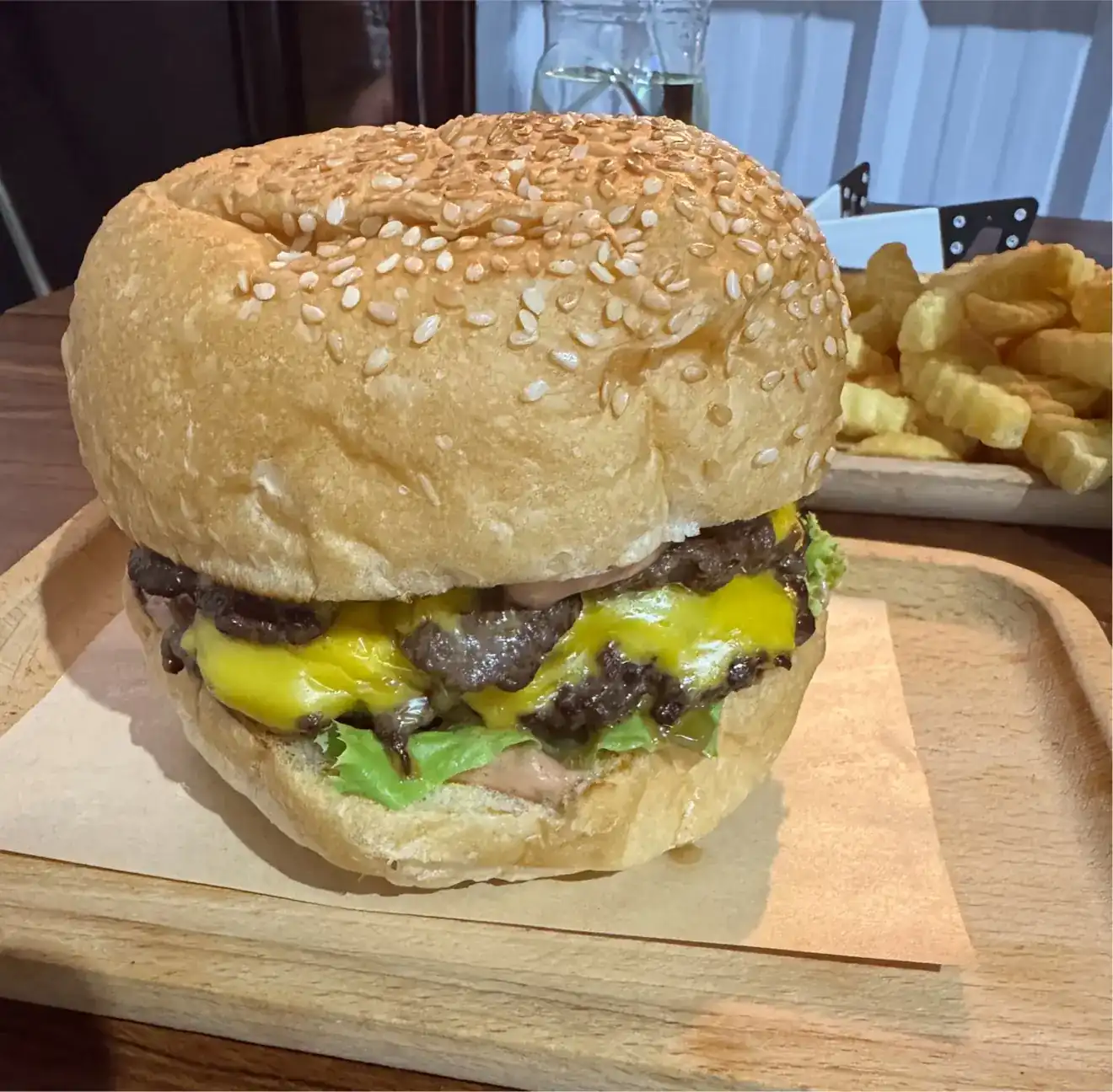 A double cheese burger: two beef patties, melted cheese and lettuce in a sesame bun, crinkle-cut fries behind