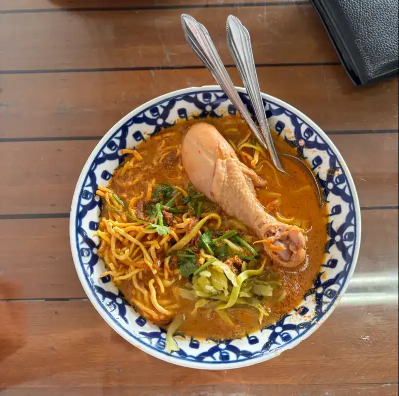 Khao soi with a chicken drumstick, egg noodles and pickled greens in a blue-and-white bowl
