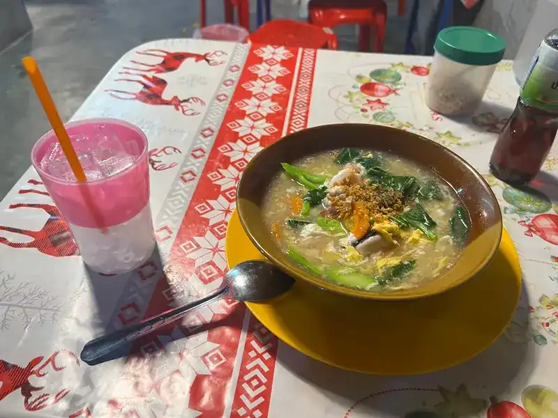 A bowl in thick gravy with greens and fried garlic, next to a pink iced drink