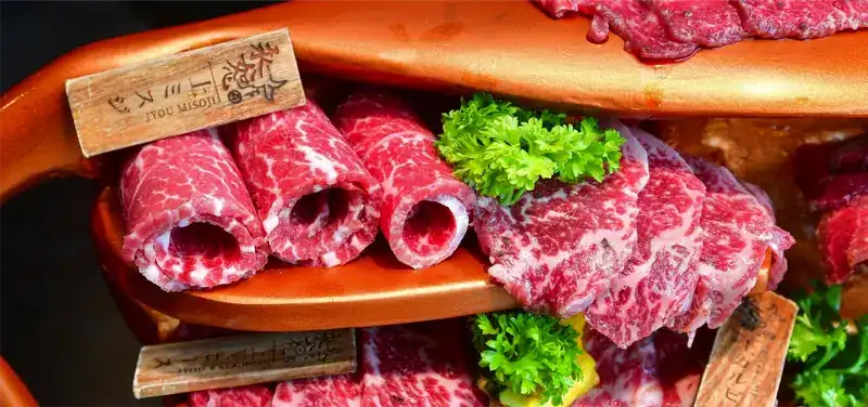 Rolled and folded slices of marbled beef on a bronze shelf, with parsley and small wooden name tags