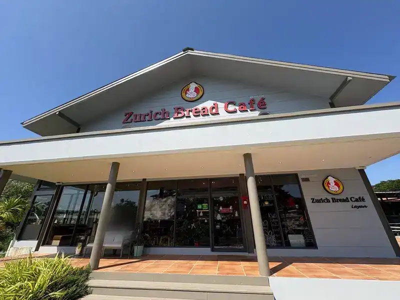 The front of Zurich Bread Café Layan: a white gabled building with the red sign and a tiled terrace