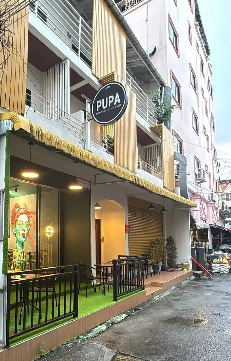 The Pupa Cafe shopfront with its round sign and a small terrace on green turf