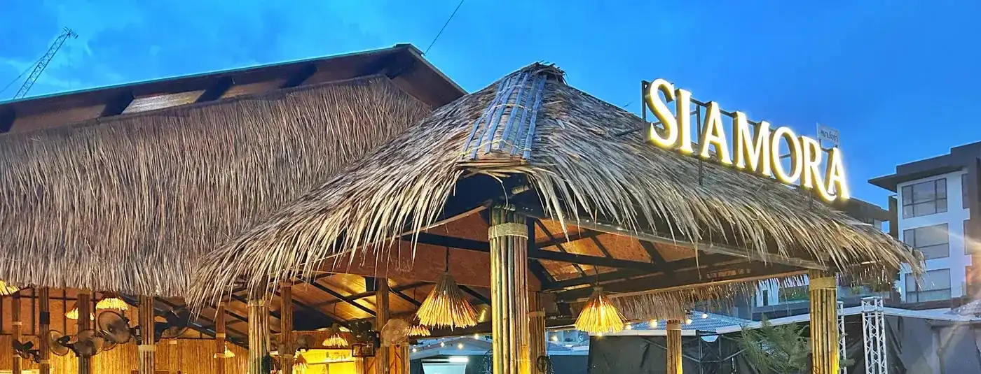 The thatched roof and lit SIAMORA sign against a deep blue evening sky