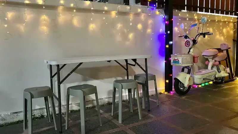 Fairy lights along the white wall above a folding table and grey stools